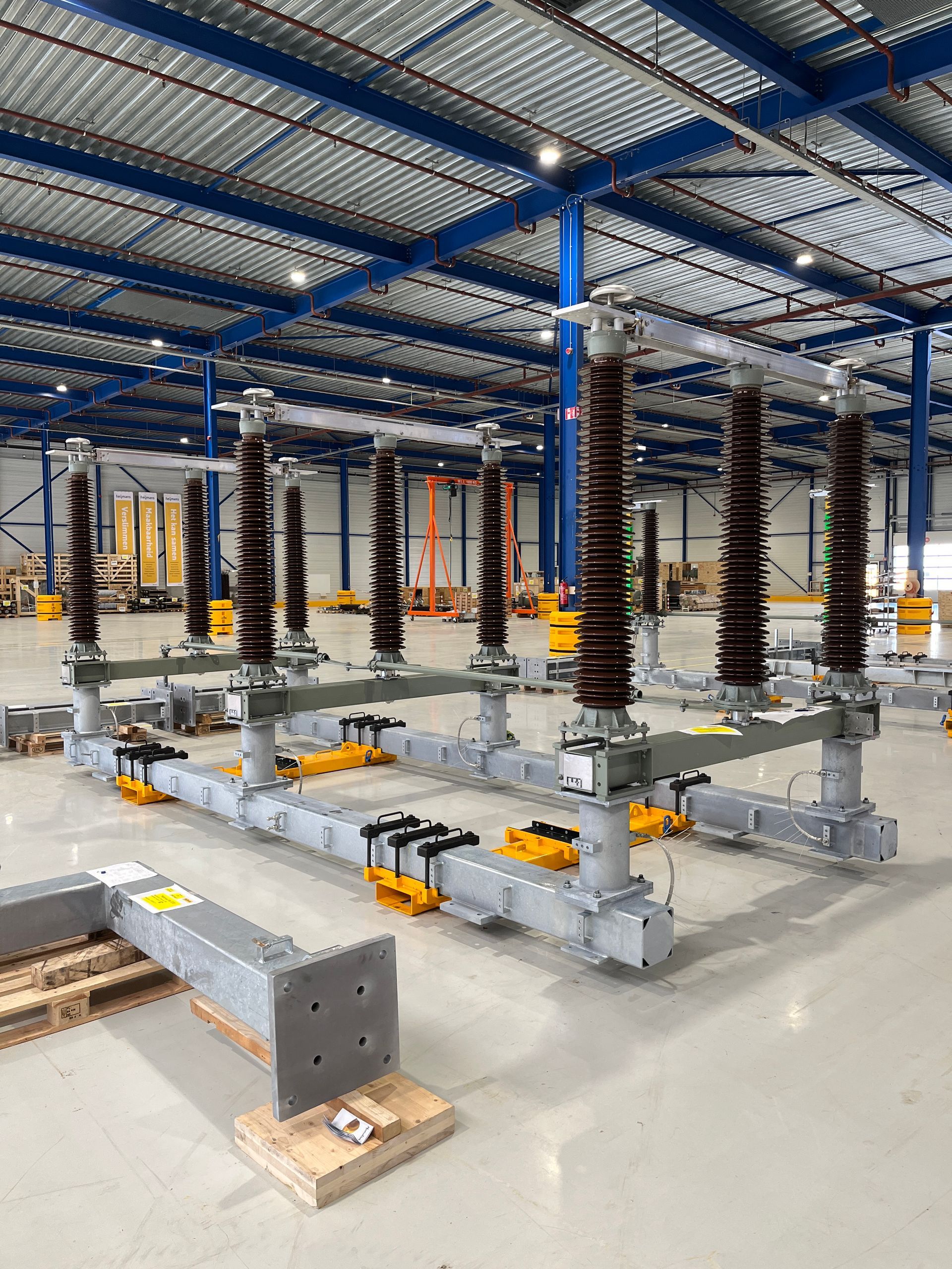 Industrieel onderstation met elektrische schakelapparatuur, grijze platforms en hoge zwarte isolatoren onder een blauw dak.