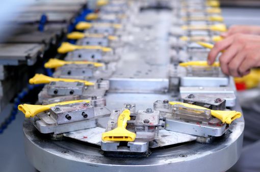 Een lopende band met metalen onderdelen met gele handgrepen wordt door een medewerker met de hand gemonteerd.
