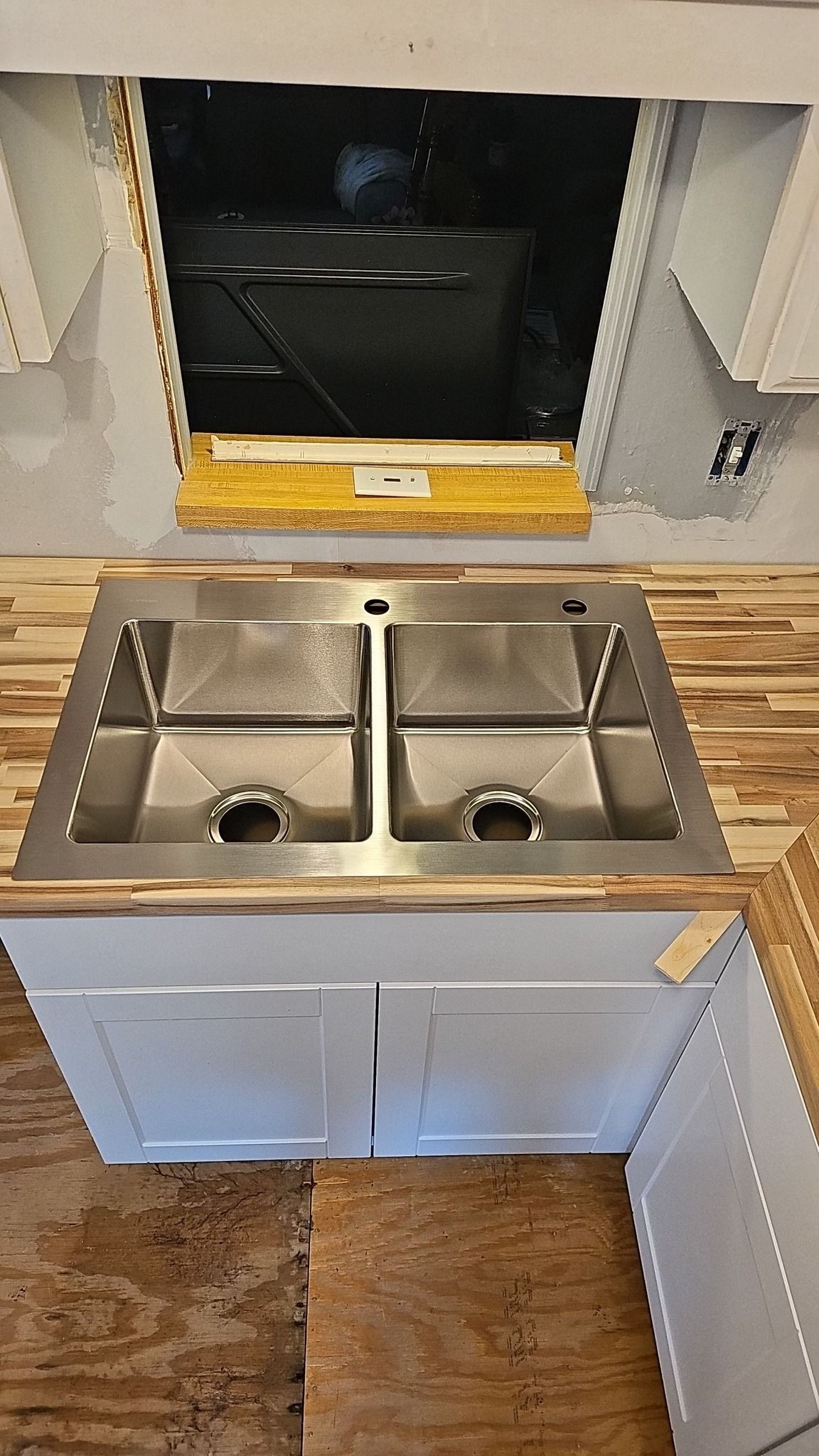 Compact kitchen with stainless steel double sink and white cabinets under a window.