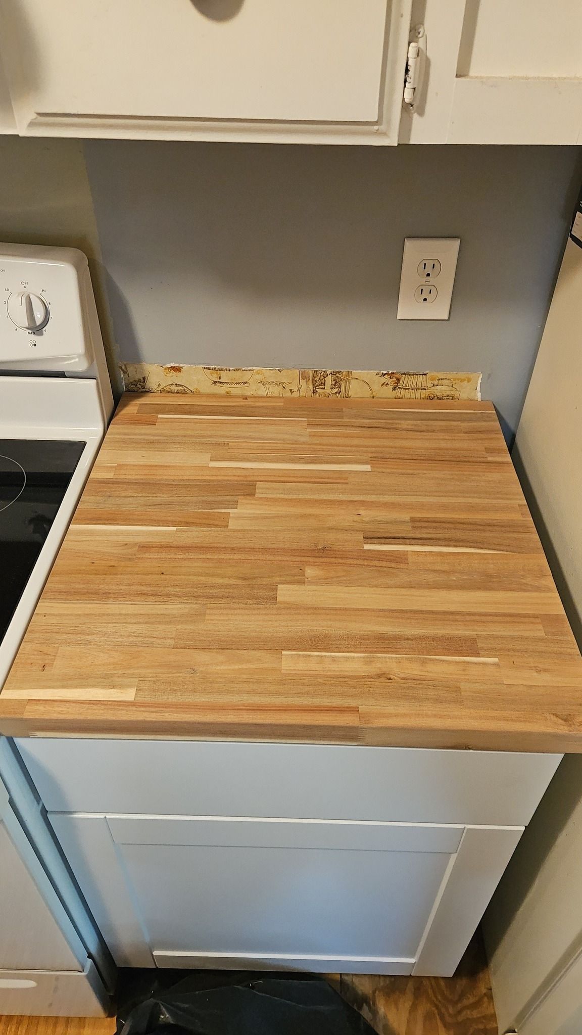 Kitchen countertop with a butcher-block cutting board beside a dishwasher and outlet.