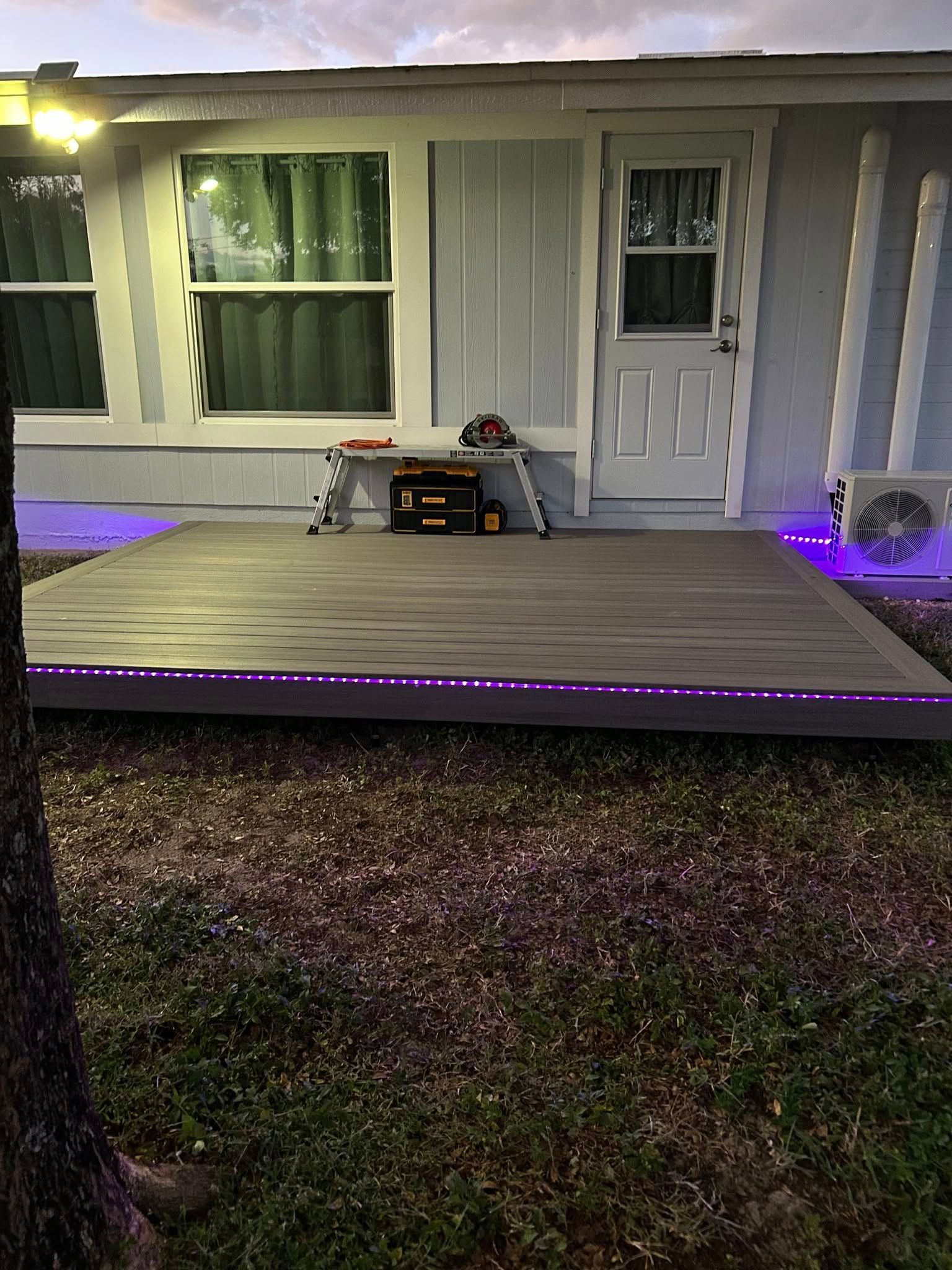 Front porch with gray siding, white door, windows, and purple LED lights along the deck edge.