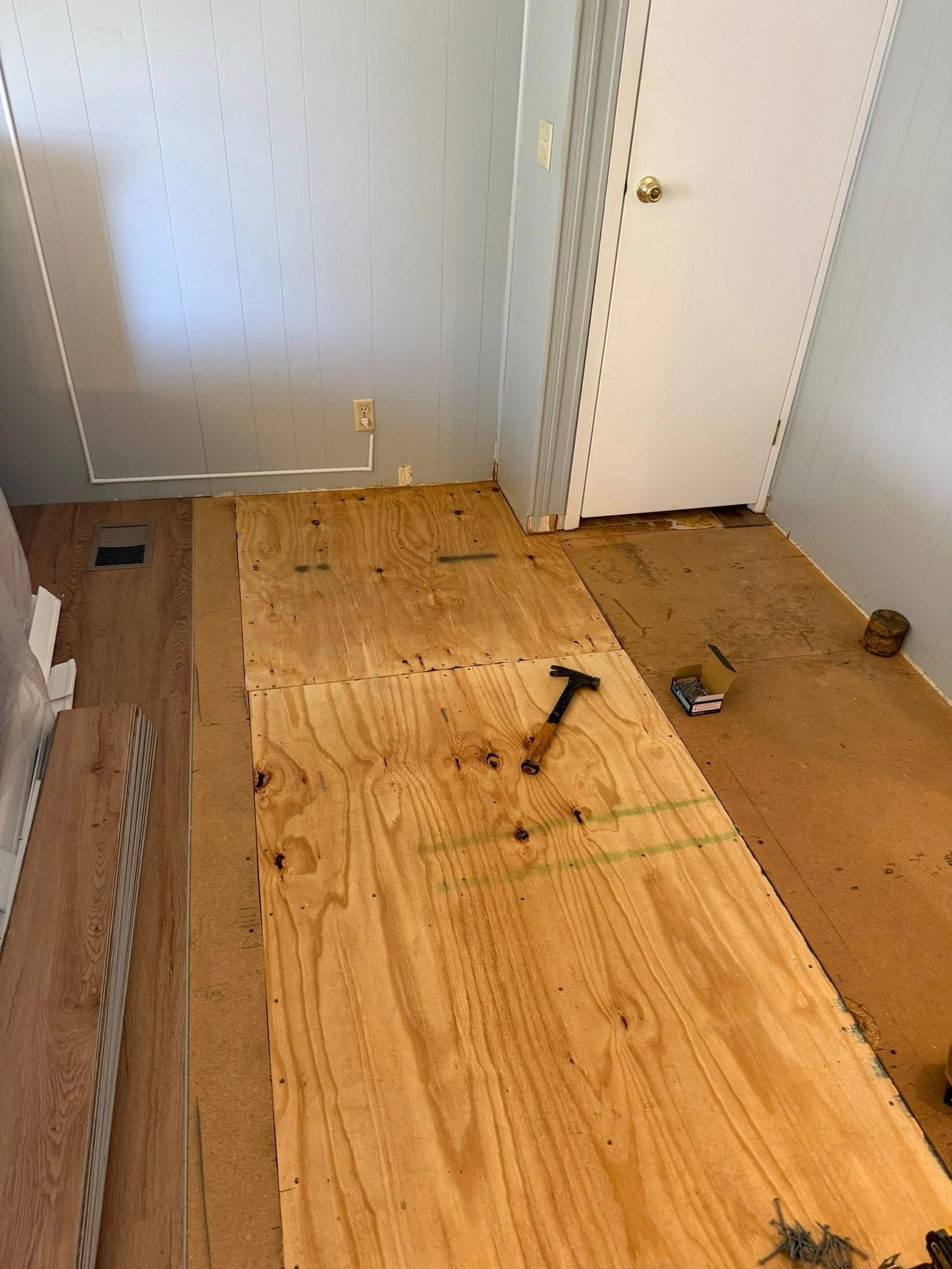 Partially removed wood floor in a hallway with tools and exposed subfloor near a white door