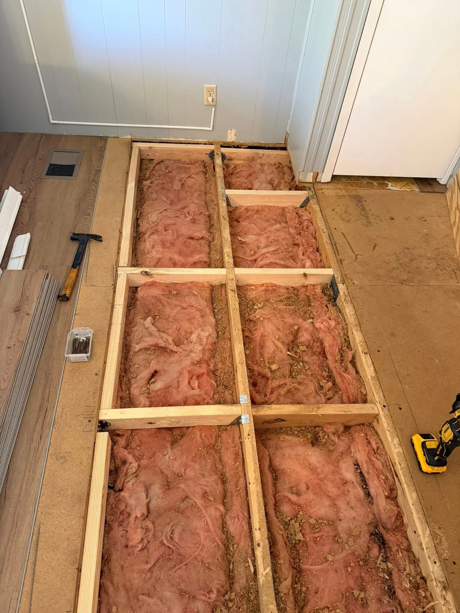 Partially framed floor with pink insulation in a room under renovation, tools on the left and a drill on the right