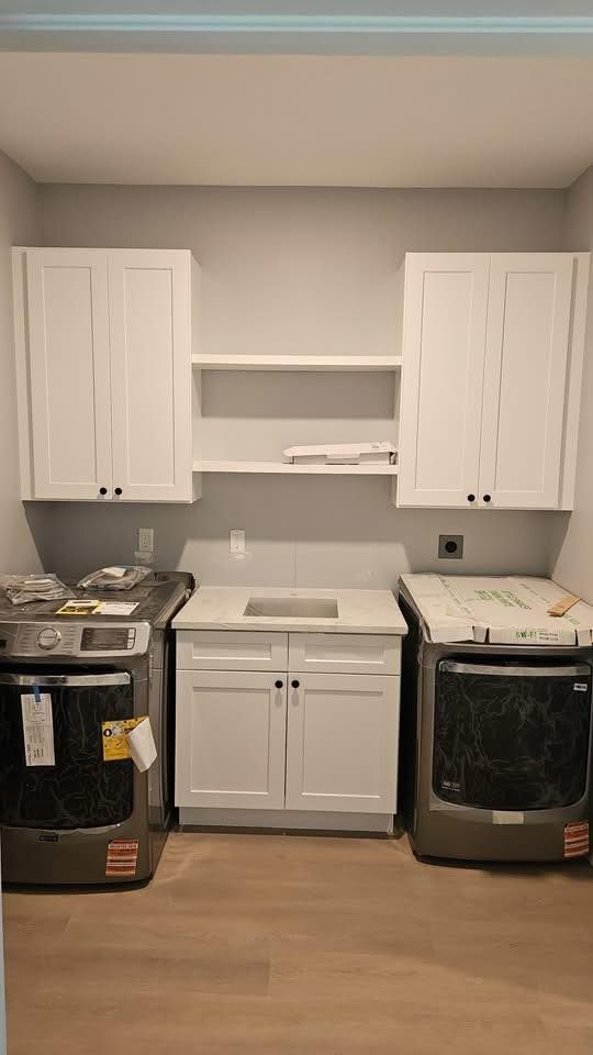 Laundry room with white cabinets, utility sink, and two washing machines against a gray wall.