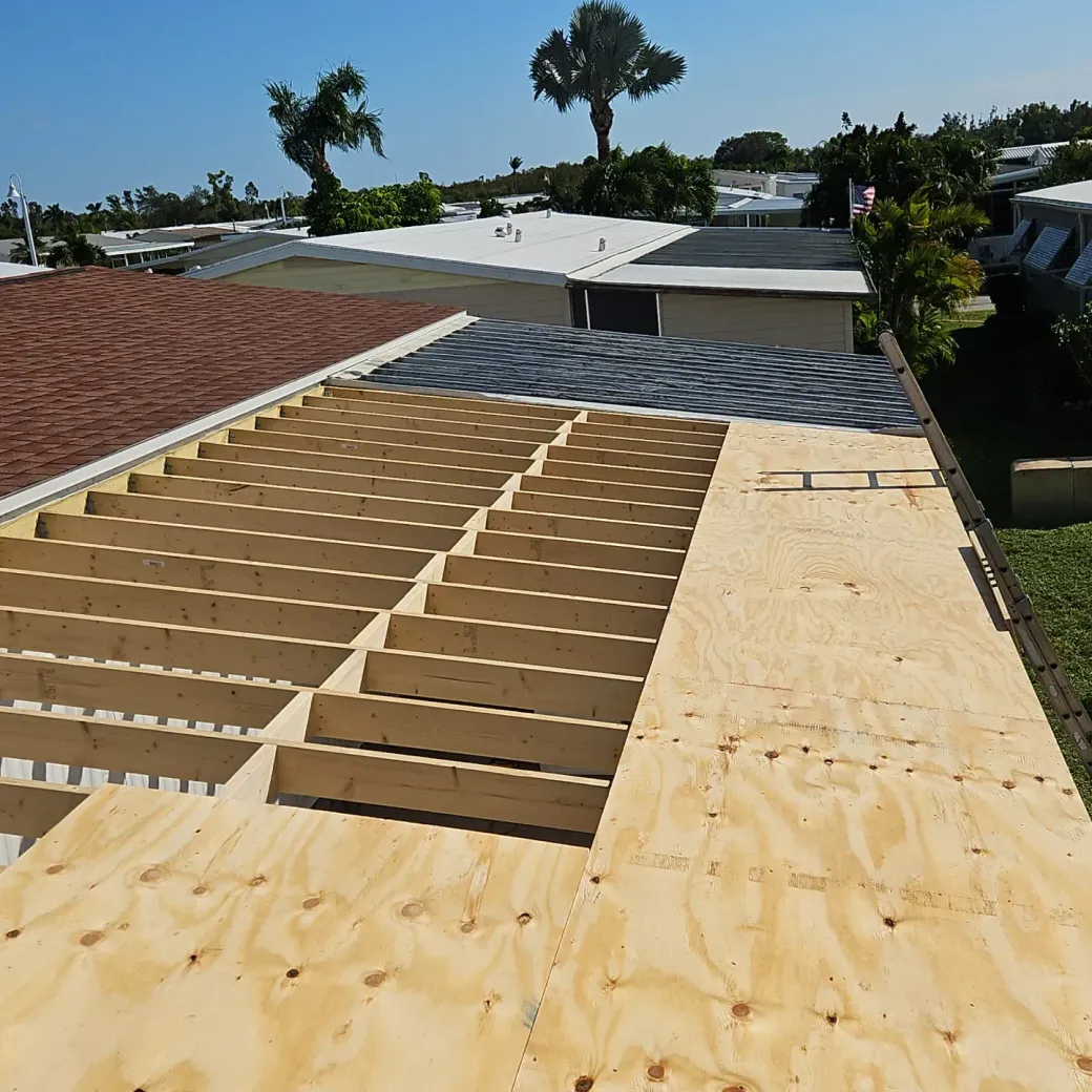 Roof under construction with exposed wooden framing and plywood sheathing on a sunny day