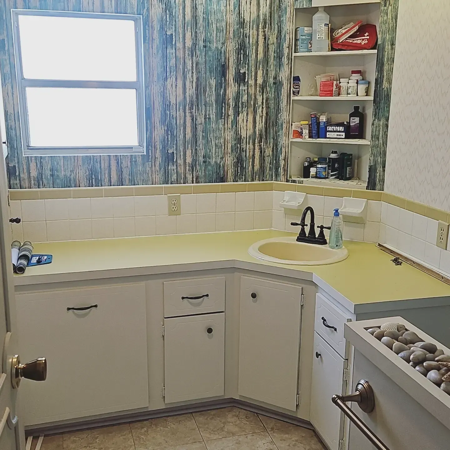 Small bathroom with white cabinets, yellow countertop, blue patterned curtains, and a sink by the window.