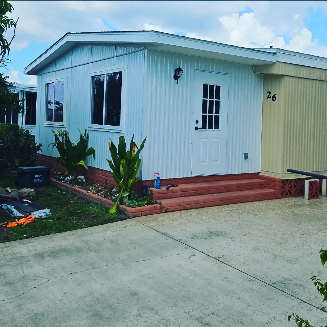 Small white house with a red porch and driveway, blue sky, and the number 26 on the side.