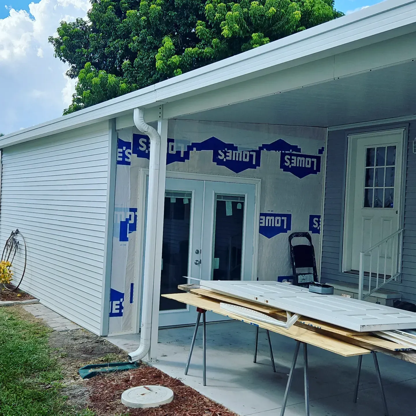 House exterior under construction with white siding, blue insulation, and a work table on the porch