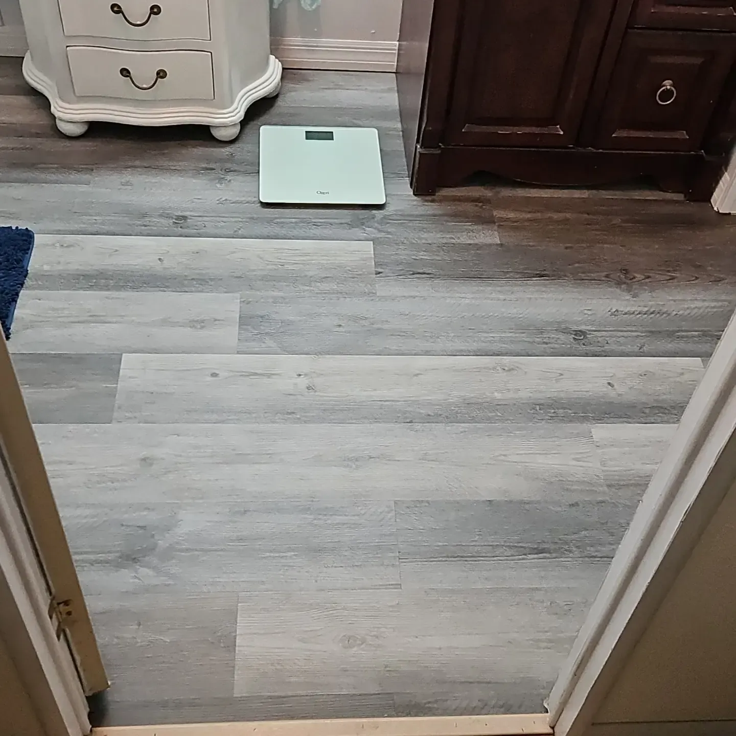 Bathroom with gray wood-look floor, white scale, and dark wood vanity near a doorway