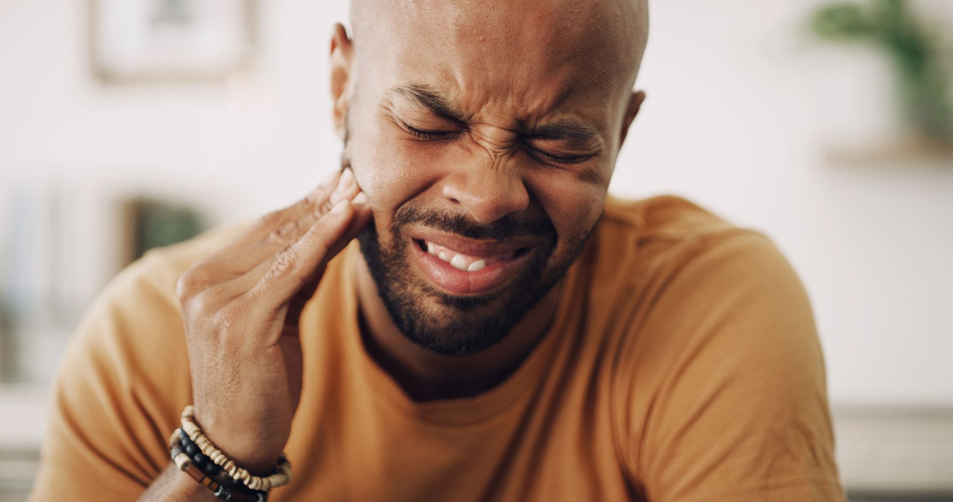 Person grimacing and holding their neck in pain indoors