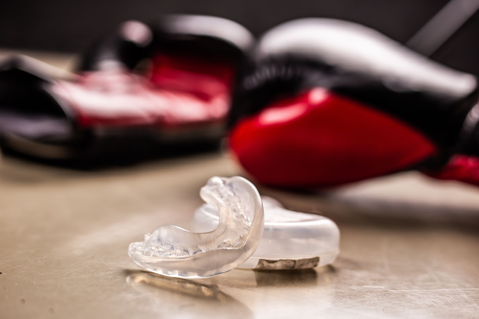 Broken clear mouthguard on a wooden floor, with blurred red and black boxing gloves in the background