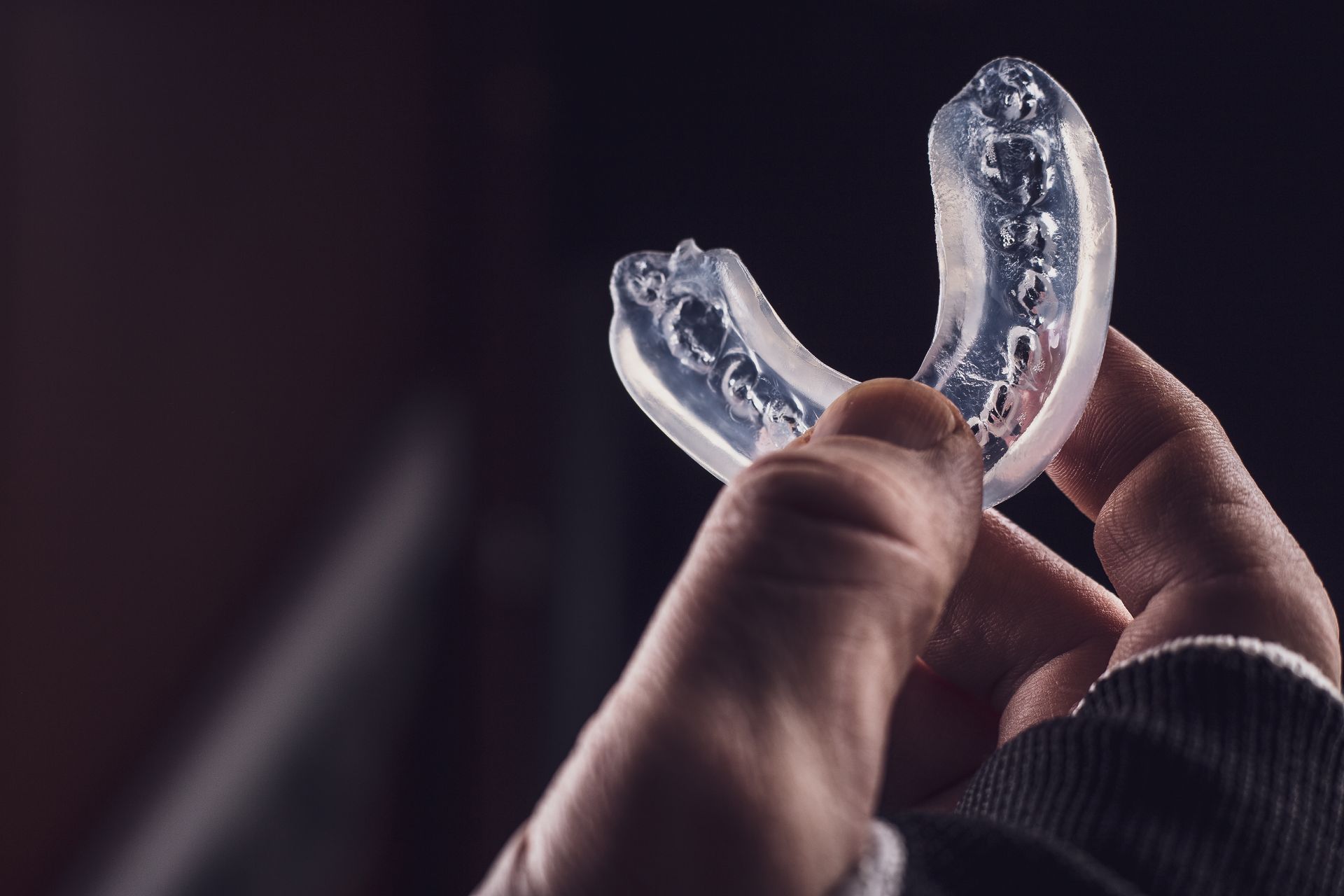 Hand holding clear dental aligners against a dark background