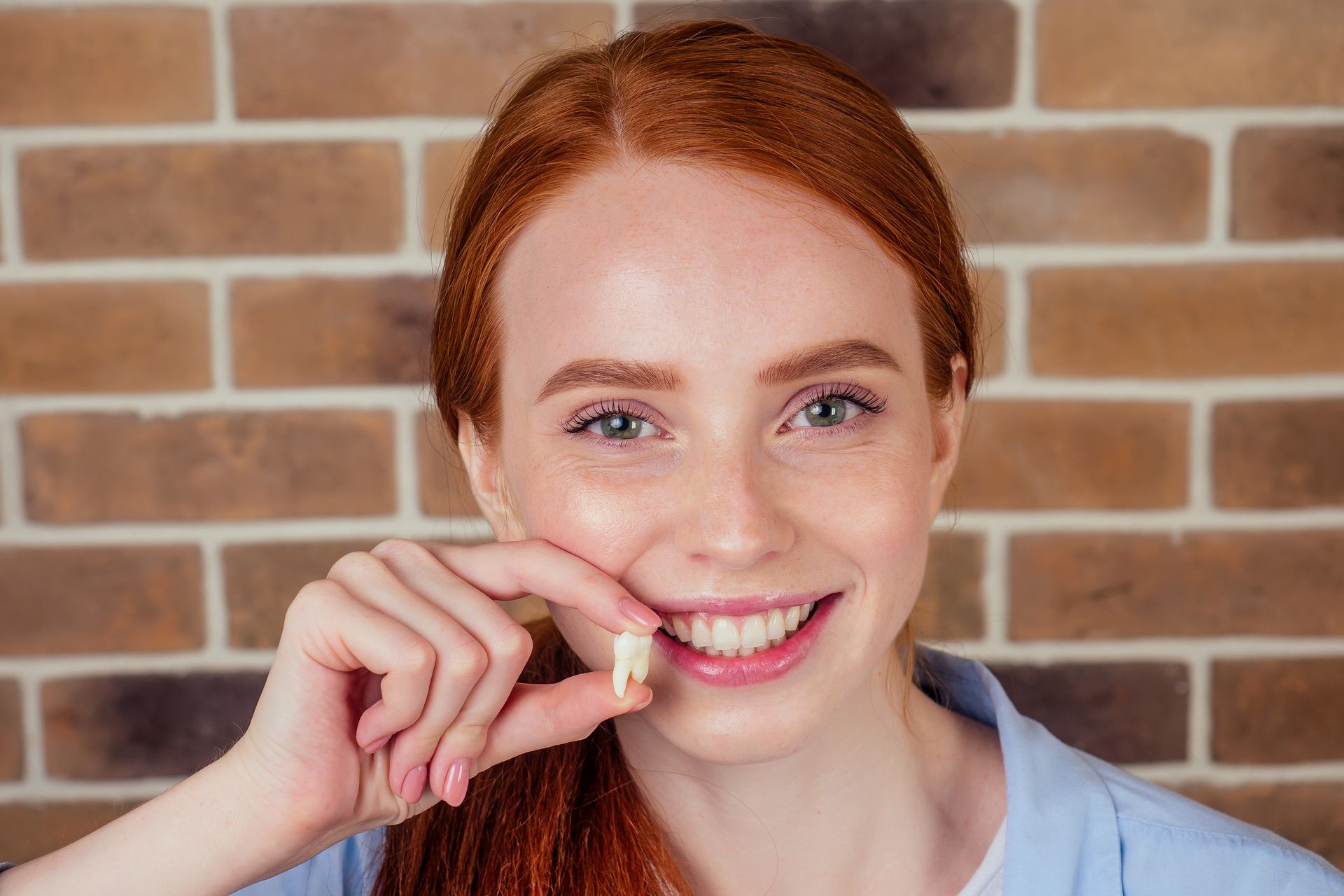 Smiling woman holding a small dental aligner in front of a brick wall