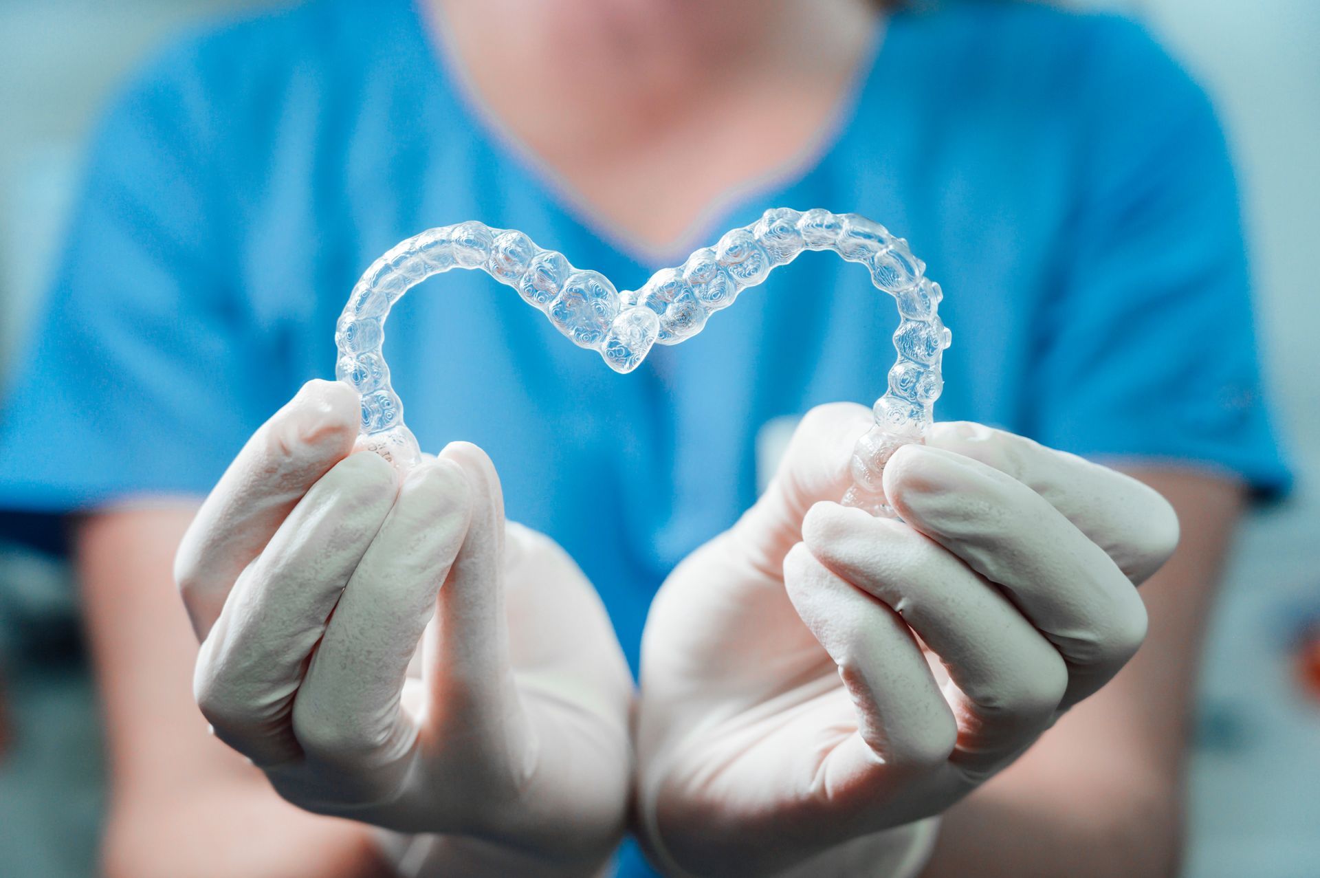 Gloved hands holding a clear transparent dental aligner against a blurred blue background