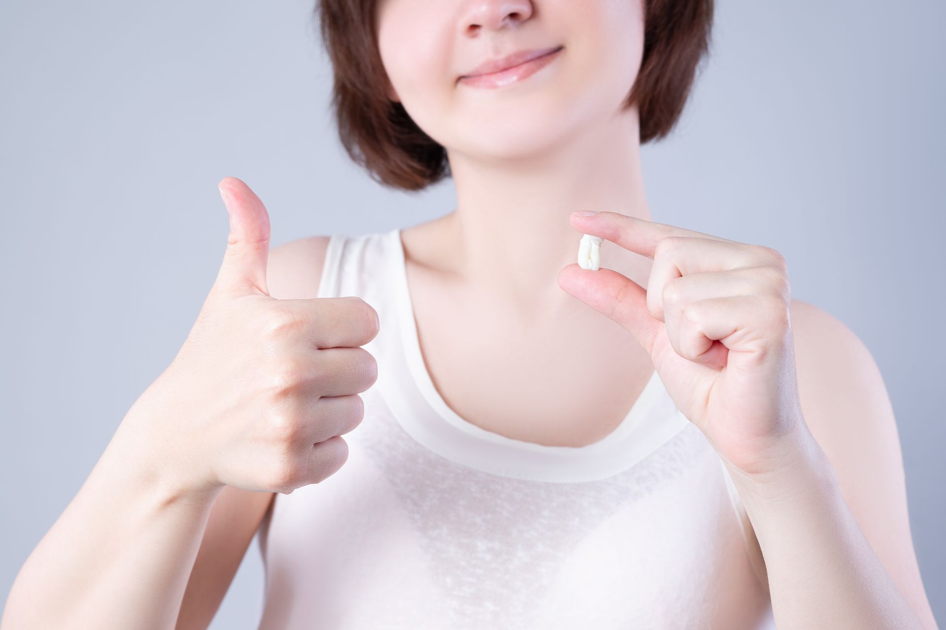 Person in a white shirt smiling and giving a thumbs-up while holding a small pill.