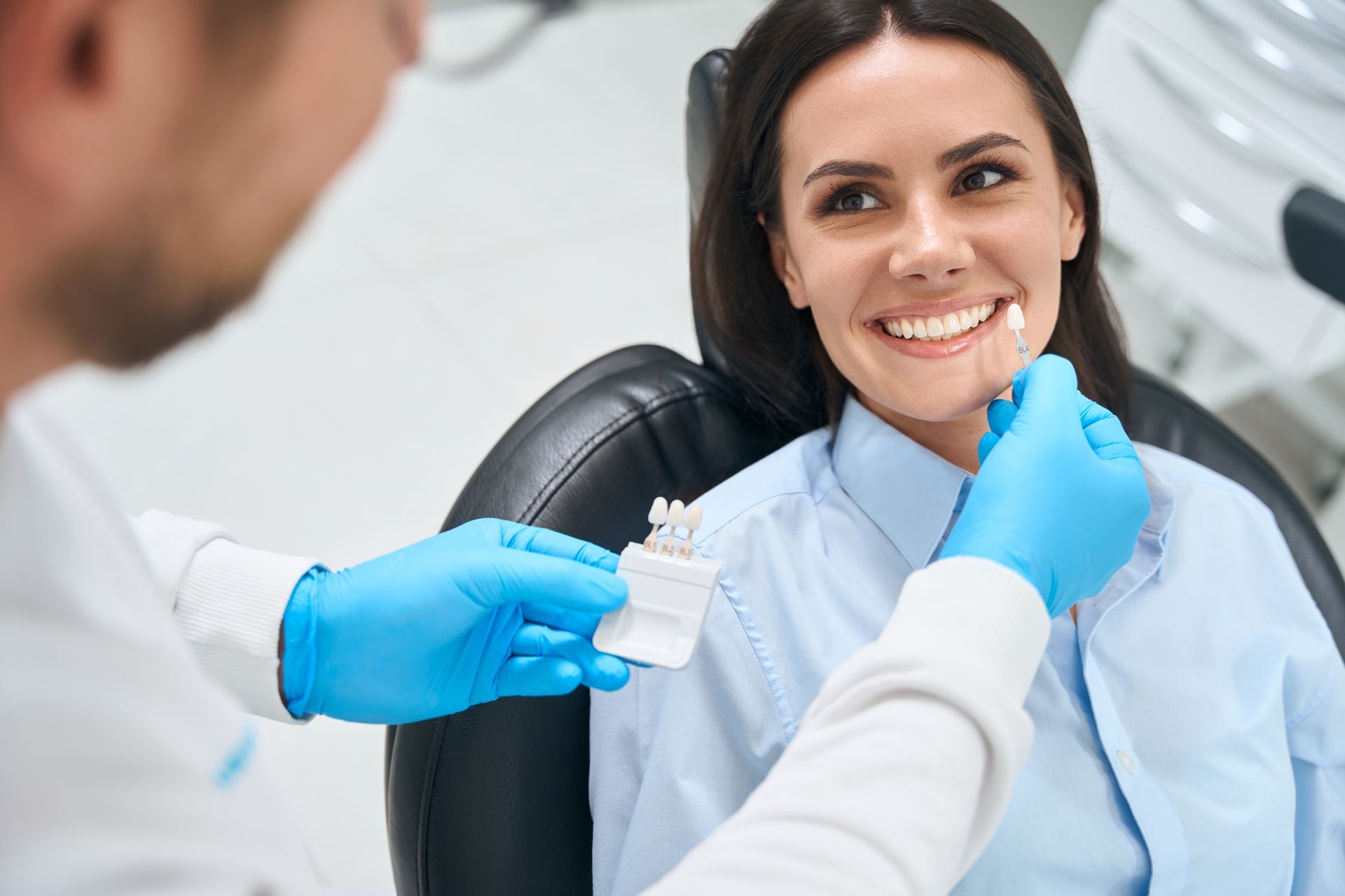 Dentist examining a smiling patient in a dental chair, with blue gloves and dental tools.
