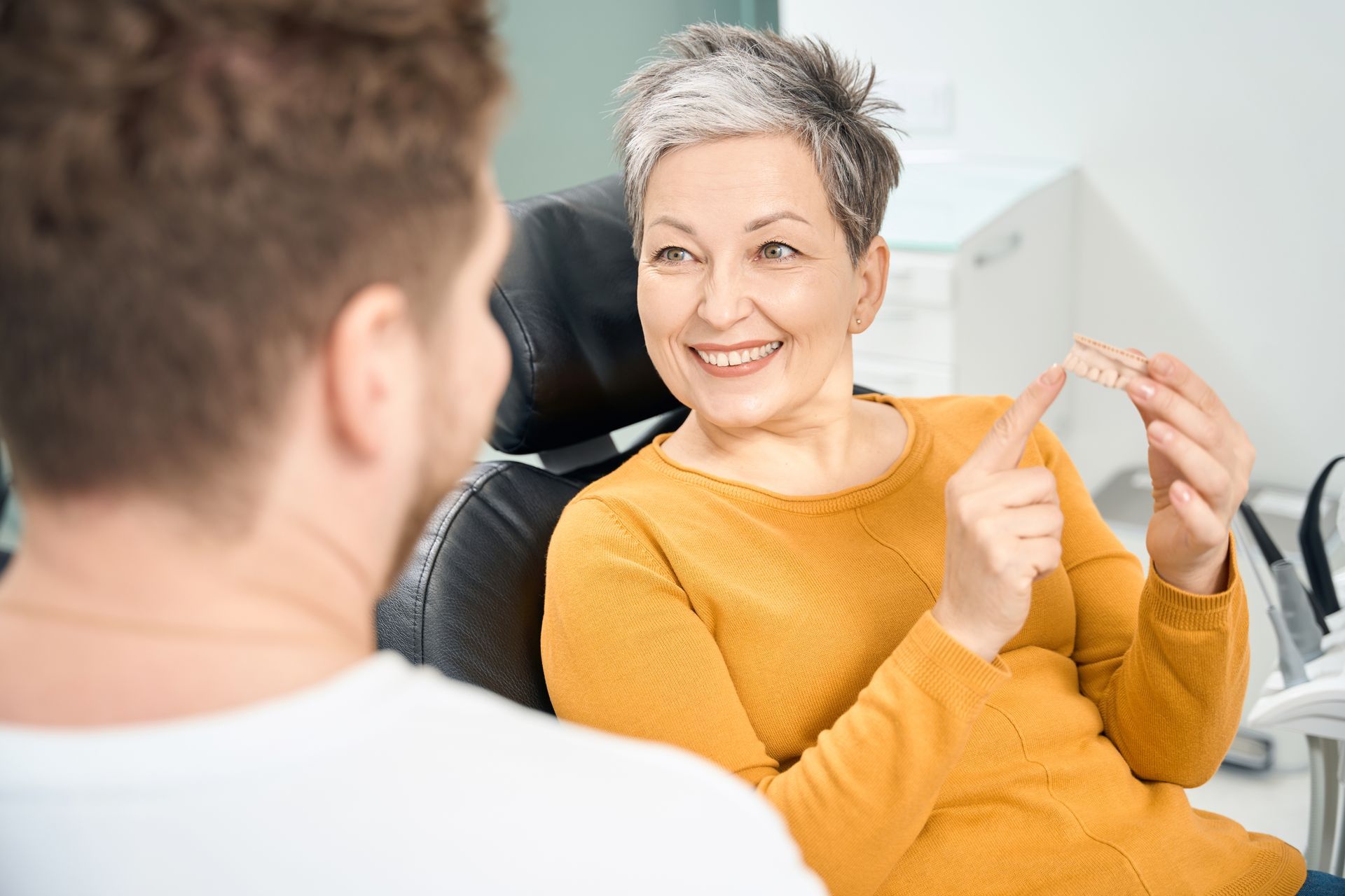 Smiling woman in a mustard sweater speaking with a man in a bright office setting