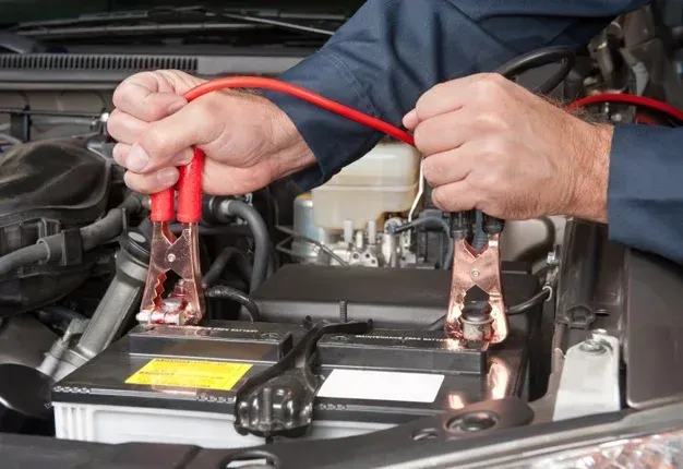 Hands using jumper cables on a car battery in an engine bay.