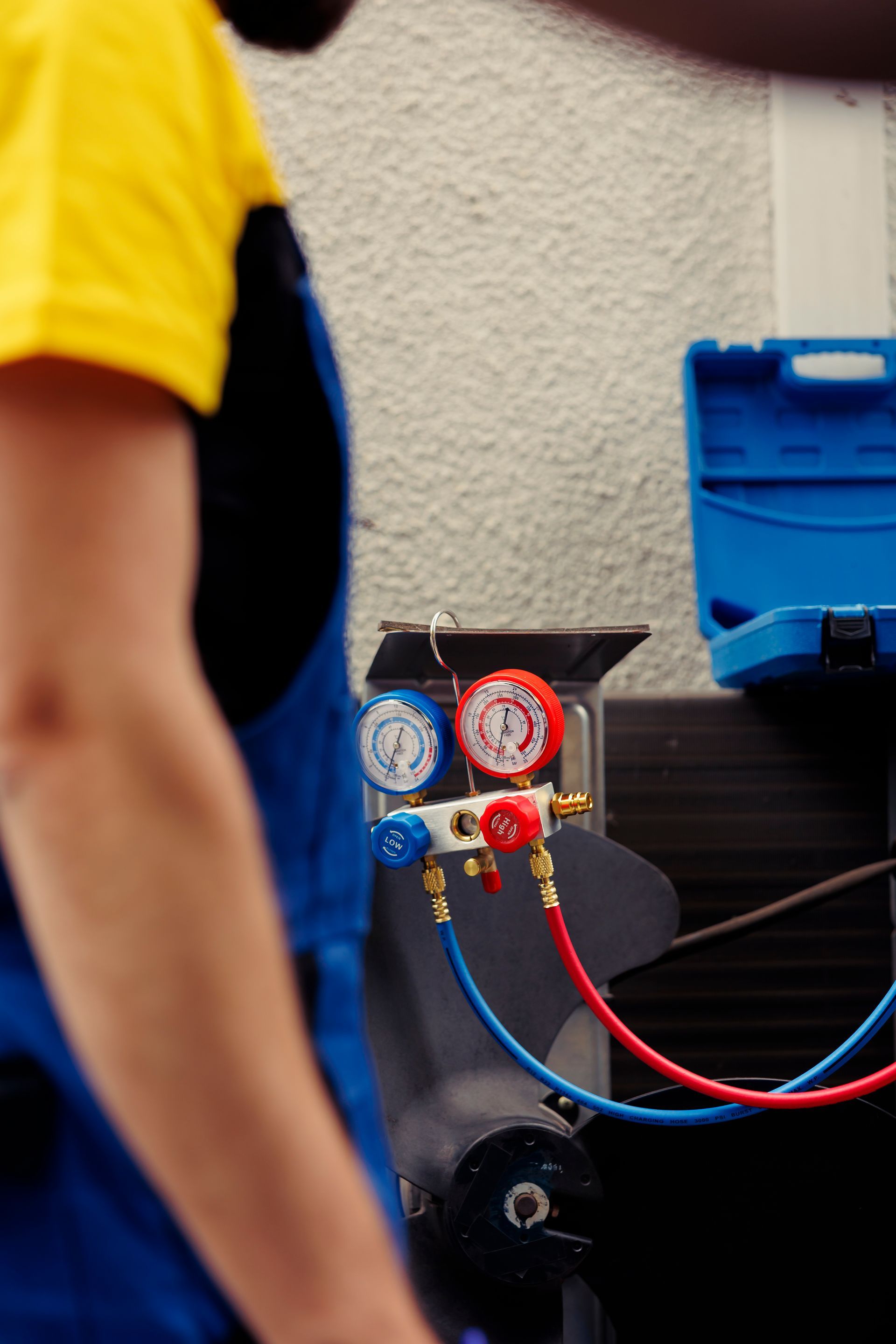 Person in yellow shirt near blue and red pressure gauges on equipment panel