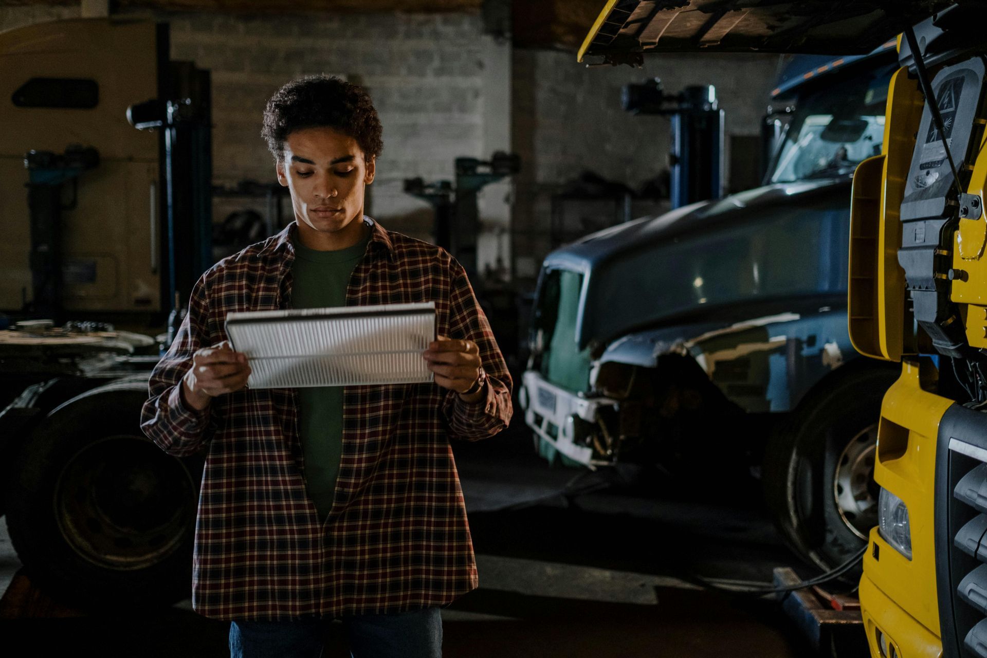 Mechanic reading a checklist in a dim auto repair shop beside a lifted vehicle and yellow lift.