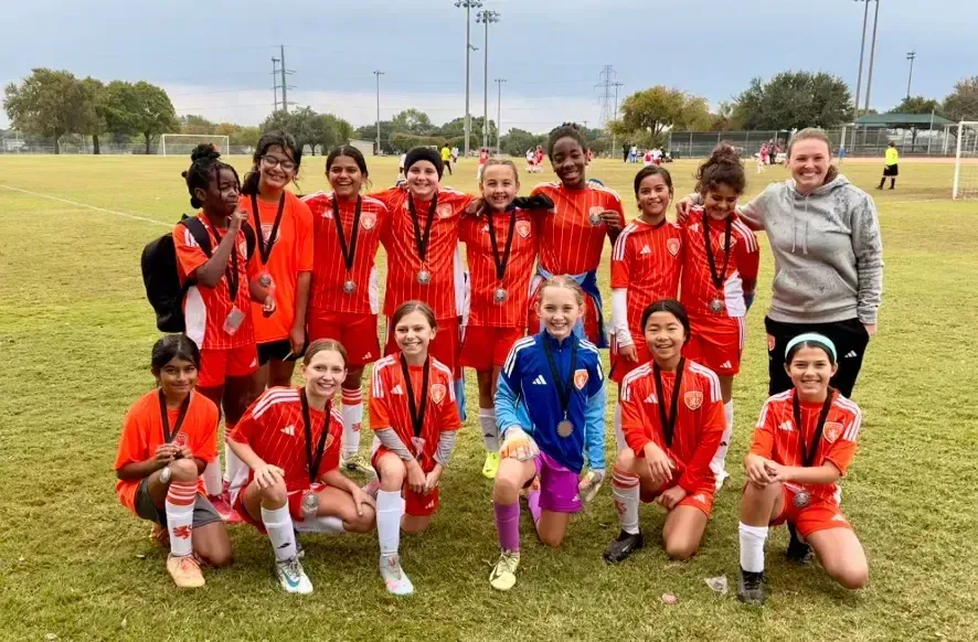Soccer team in red uniforms posing on a grassy field with medals and a trophy