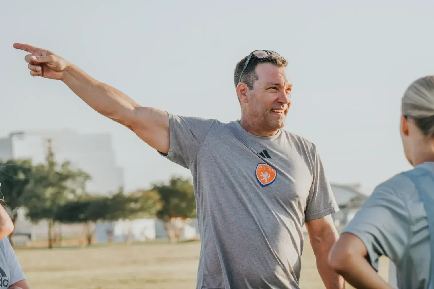 Man in gray shirt pointing across a field during an outdoor group activity