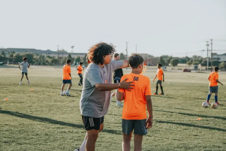 Soccer goalkeeper diving to catch a ball near the goalpost on a grassy field