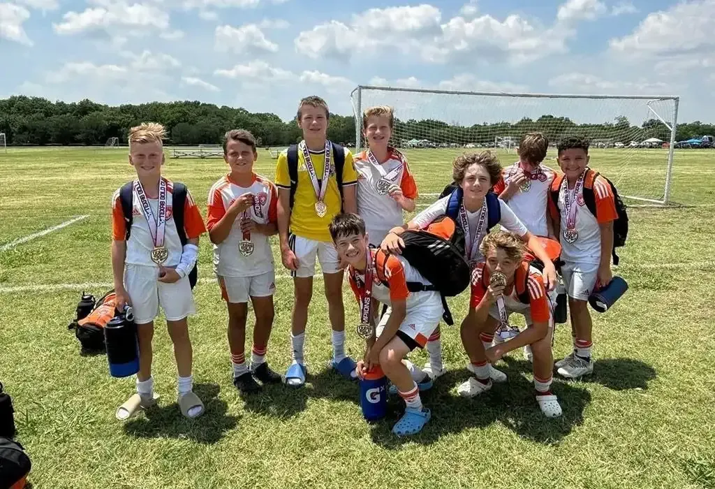Youth soccer team posing on a grassy field with medals and a goal in the background