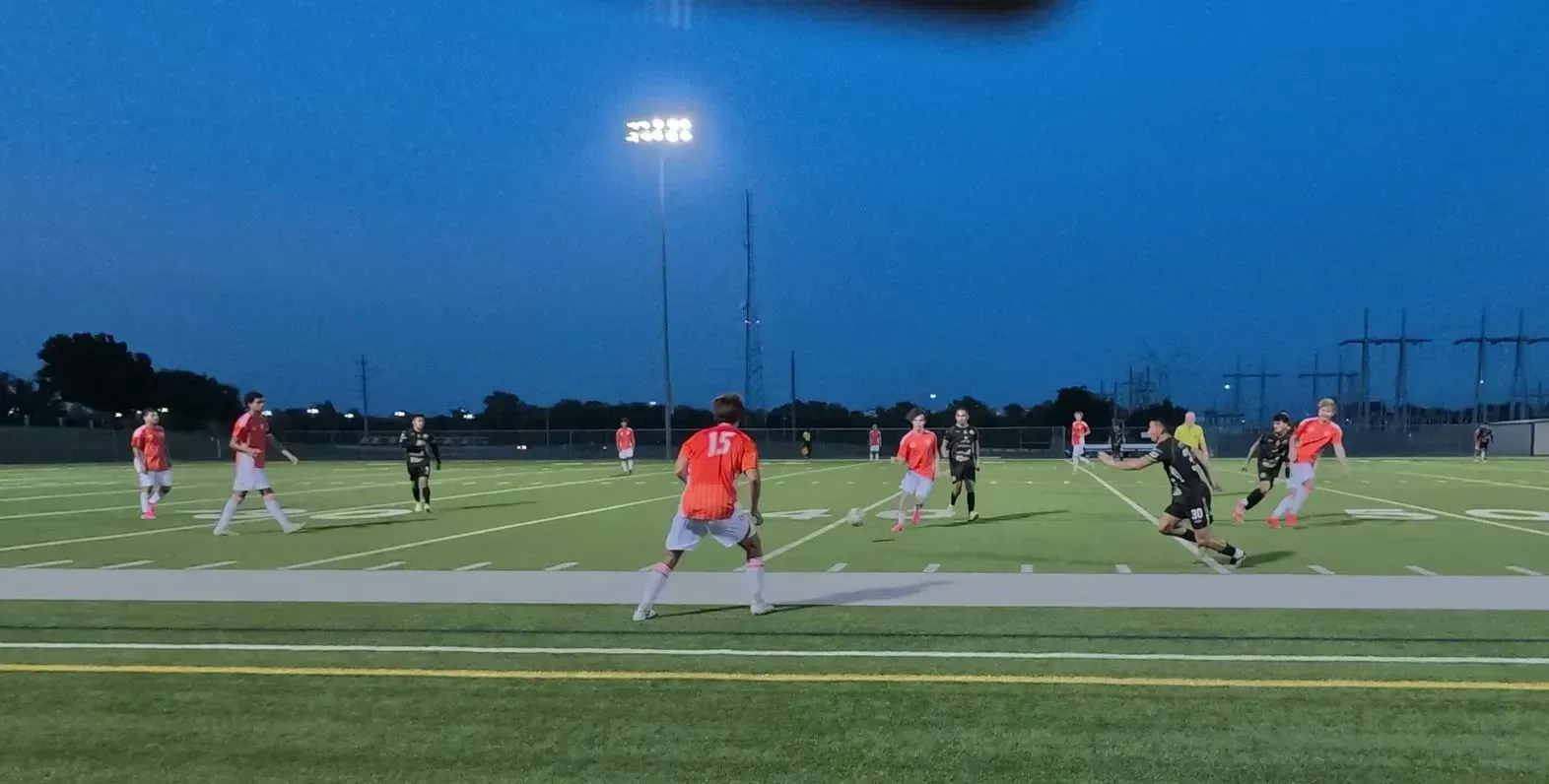Soccer players in red and black compete on a lit field at dusk