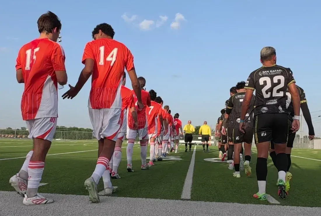 Soccer teams walk onto the field before a match, red jerseys on the left and black jerseys on the right.