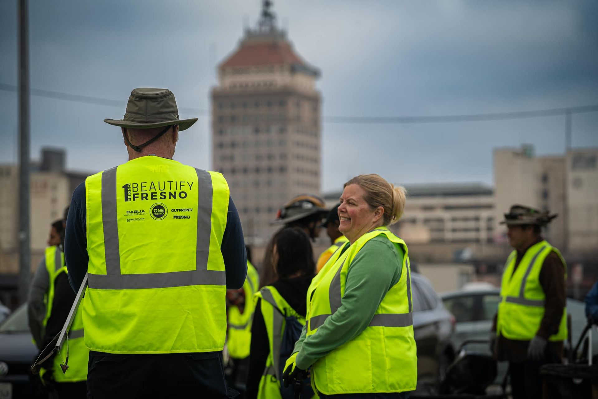 A group of people wearing yellow vests and hats are standing in front of a building.