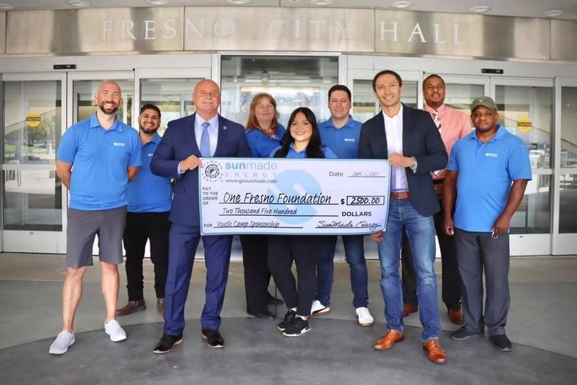 A group of people standing in front of a building holding a large check.