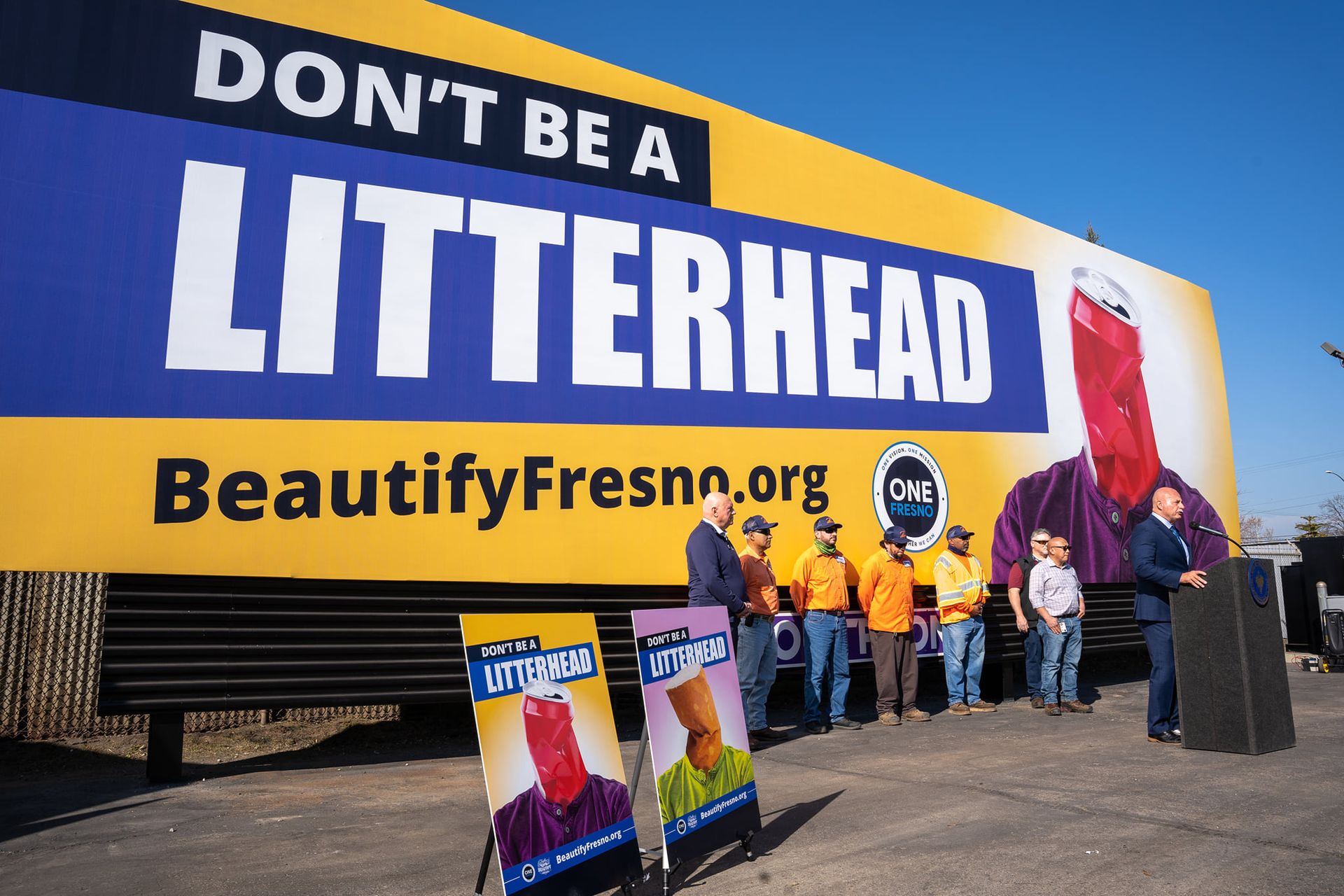 A group of people are standing in front of a large billboard that says do n't be a litterhead