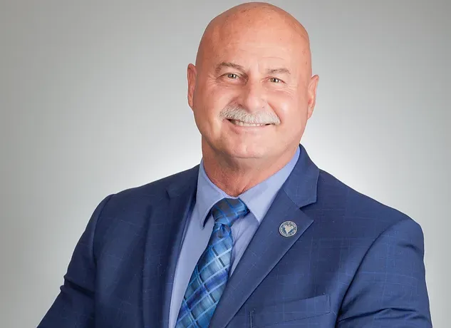A bald man in a suit and tie is smiling for the camera.