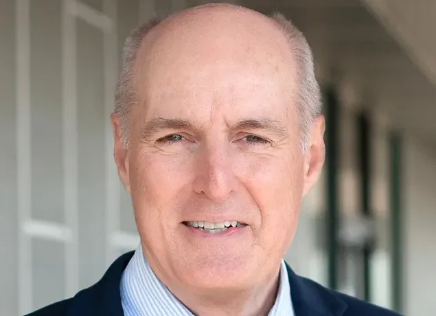 A bald man in a suit and striped shirt is smiling for the camera.