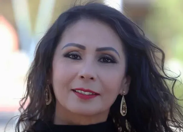 A woman with long dark hair and earrings is smiling for the camera.