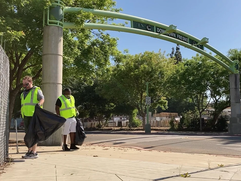 Two men are standing on a sidewalk under a green archway.