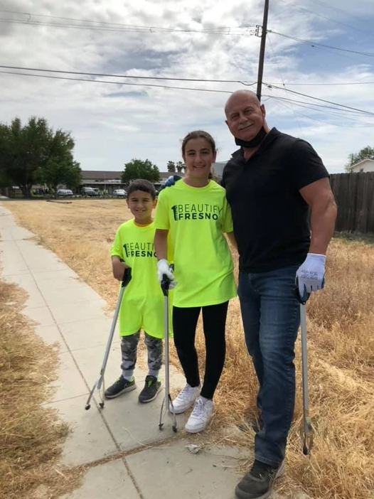 A man and two children are standing on a sidewalk holding trash cans.