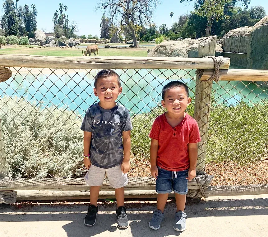 Two young boys are standing next to each other in front of a fence.