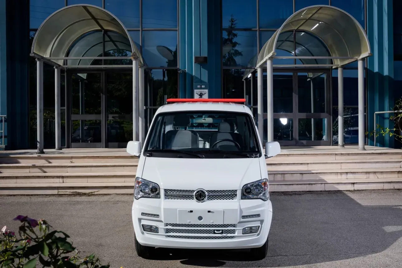 Furgone bianco parcheggiato davanti all’ingresso di un edificio, con porte a vetri e tettoie ad arco