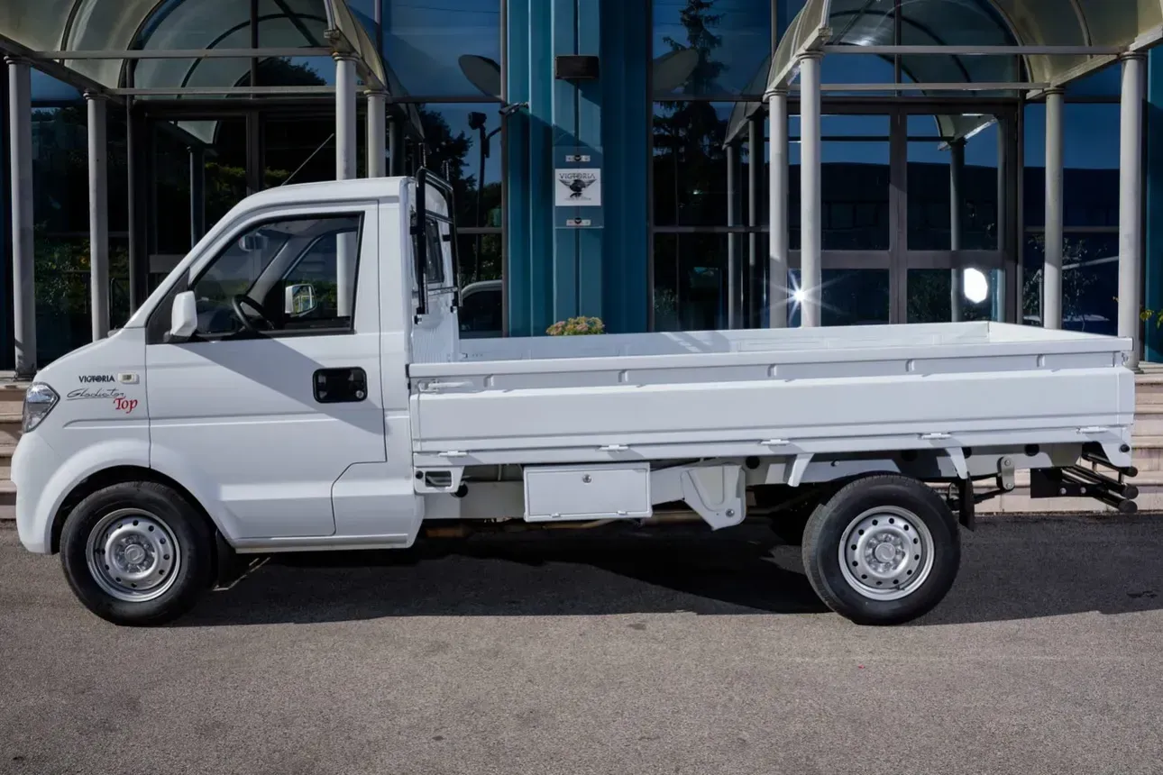 Mini camioncino a pianale bianco parcheggiato all'aperto davanti a un edificio con facciata in vetro