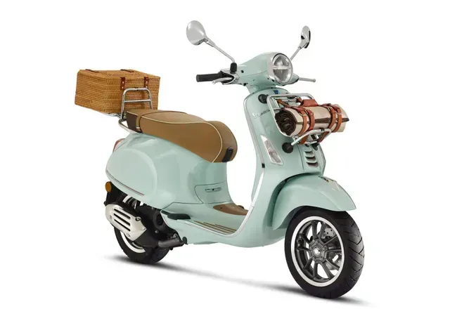 Scooter vintage azzurro chiaro con cestino in vimini e sella marrone, su sfondo bianco