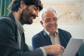 Two men looking at a tablet, one pointing at the screen, both smiling.