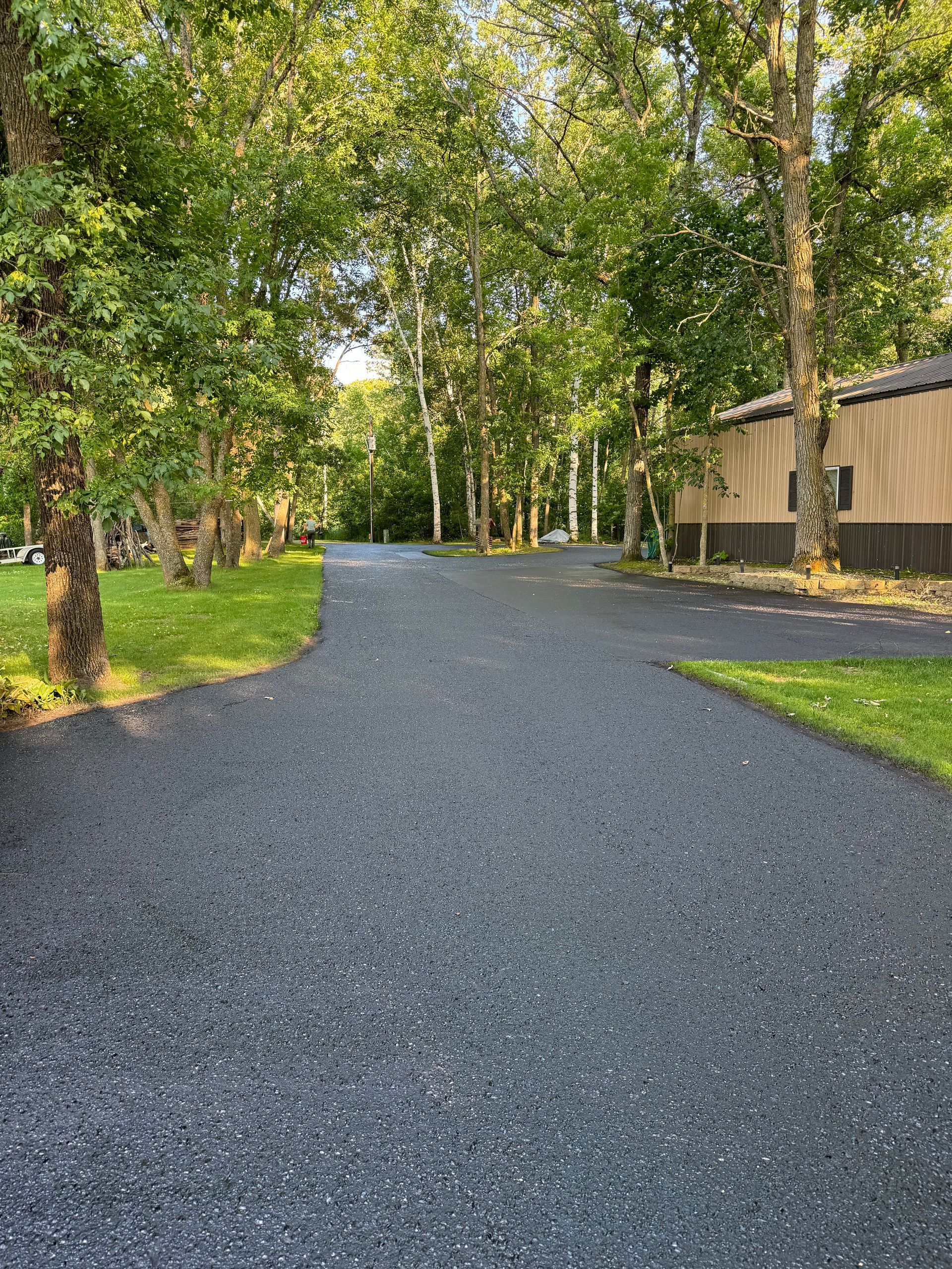 A gravel driveway leading to a house surrounded by trees and grass.