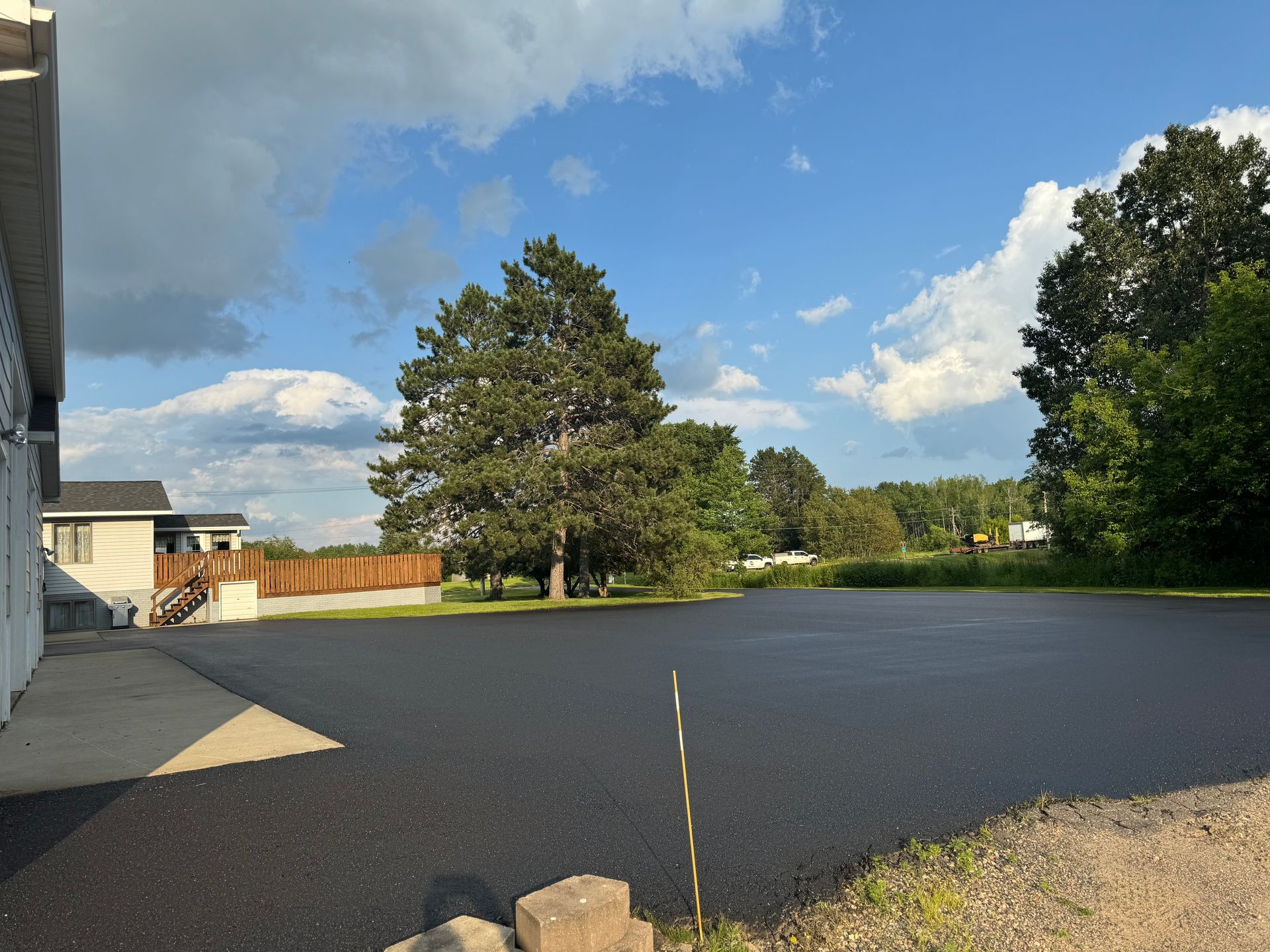 A large asphalt driveway with a house in the background and trees in the foreground.