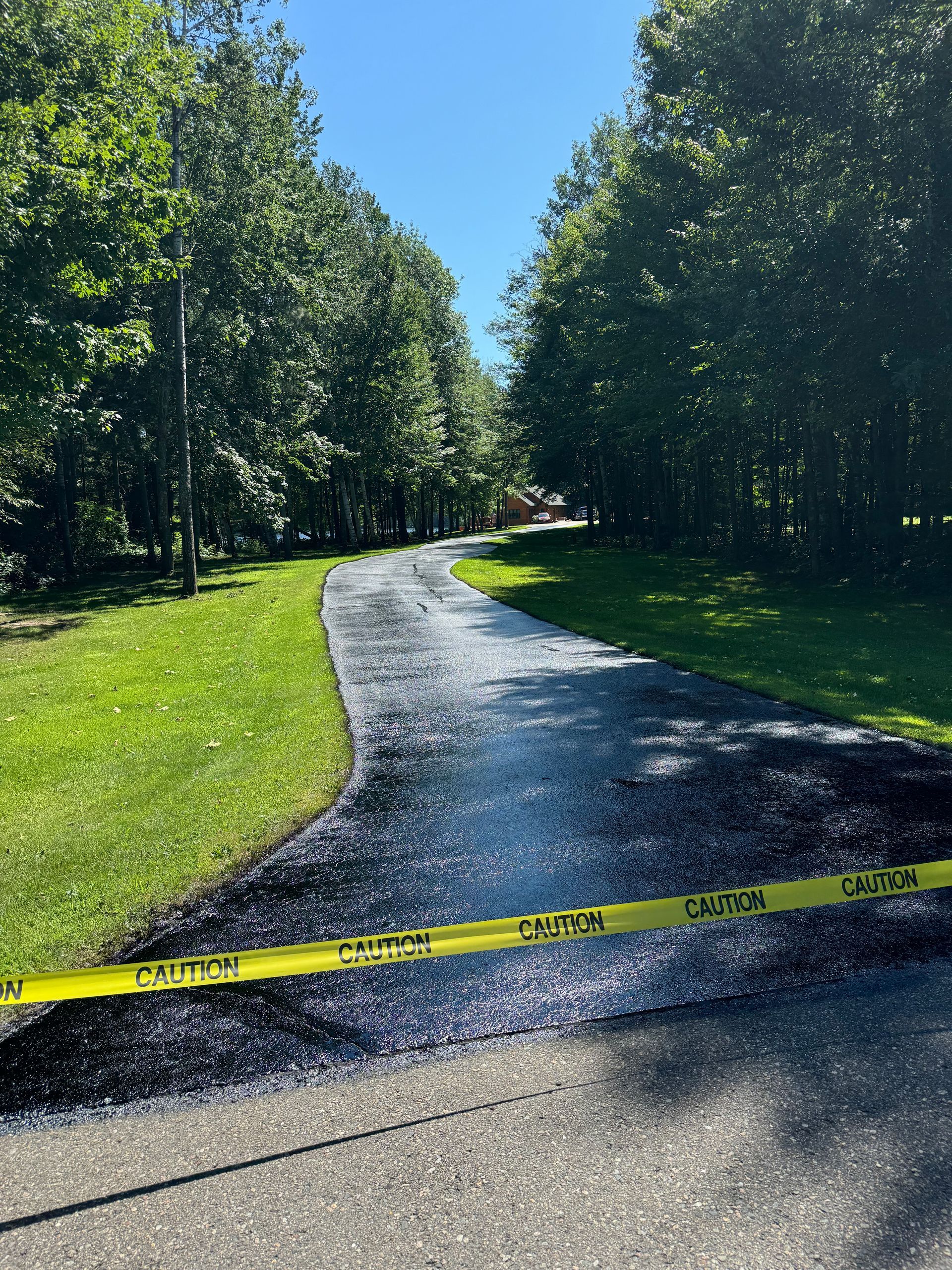 A newly paved driveway surrounded by trees and grass.