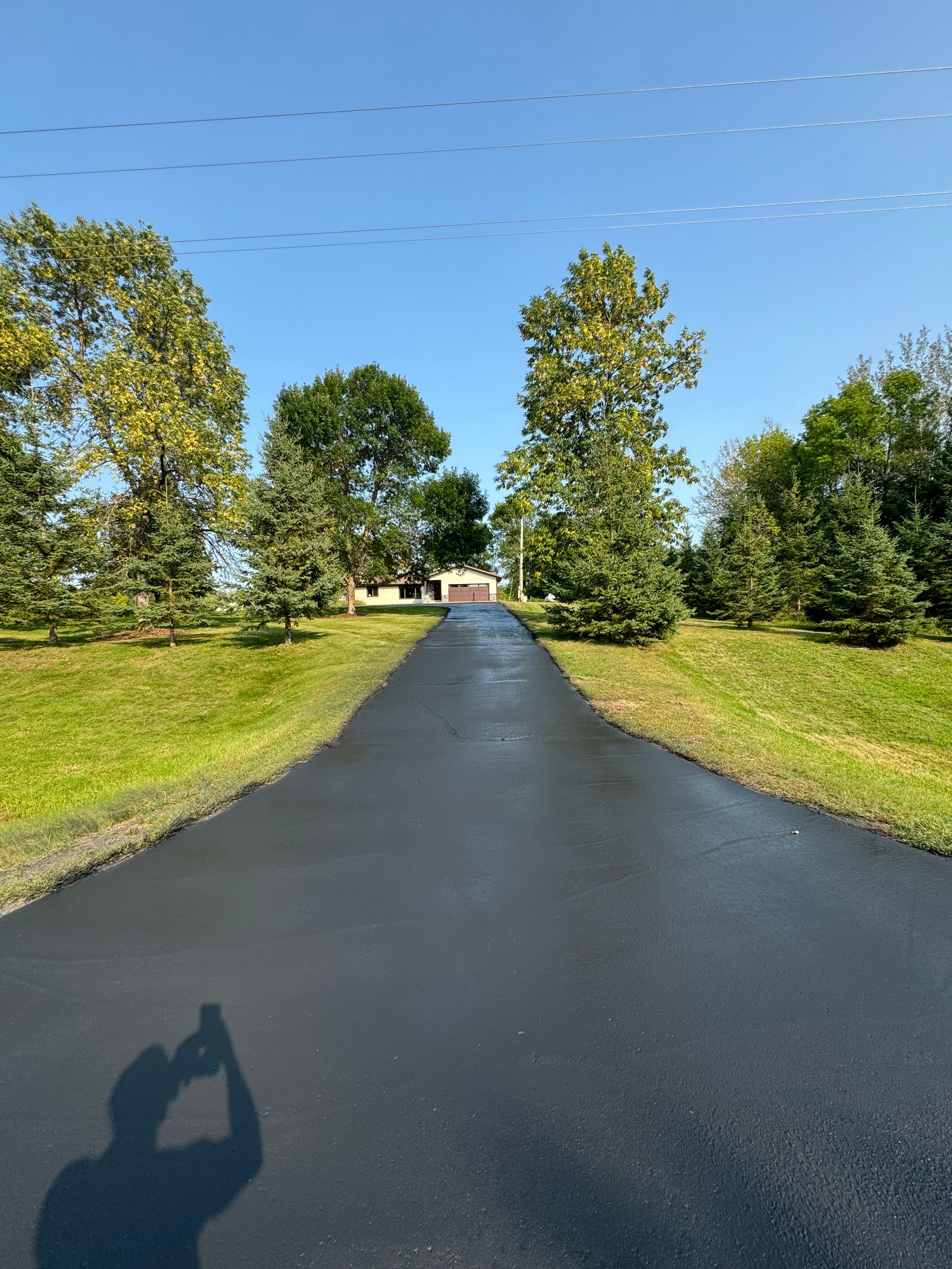 A shadow of a person taking a picture of a driveway leading to a house.