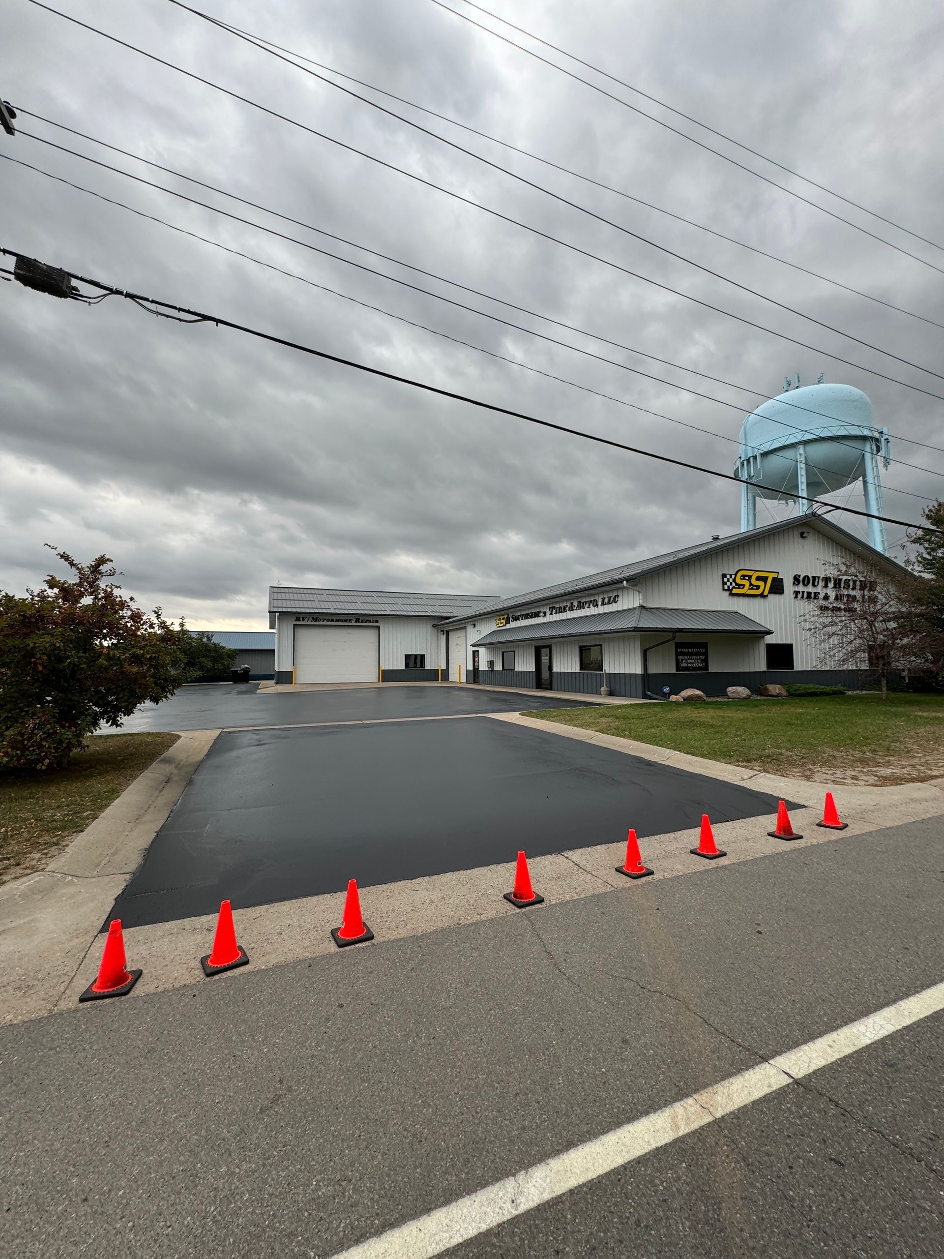 A building with a water tower in the background and a lot of orange cones on the side of the road.