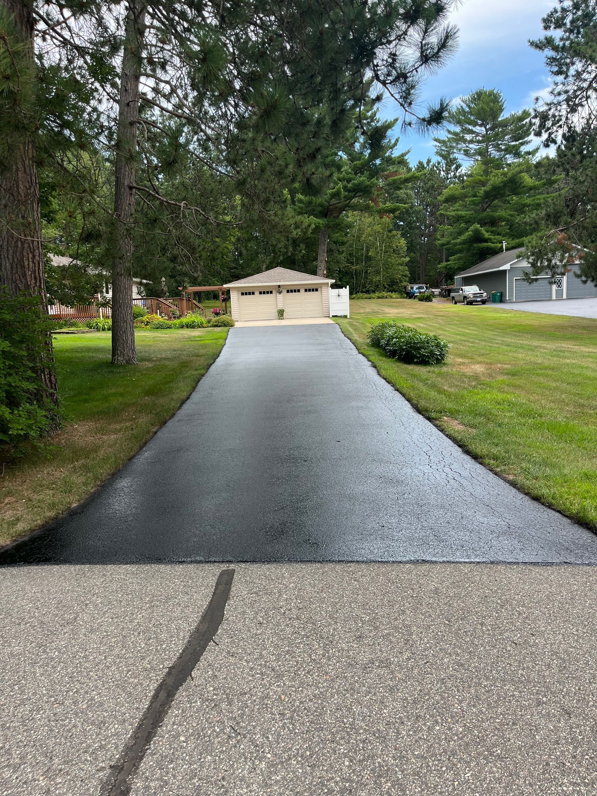 A newly paved driveway leading to a house surrounded by trees and grass.