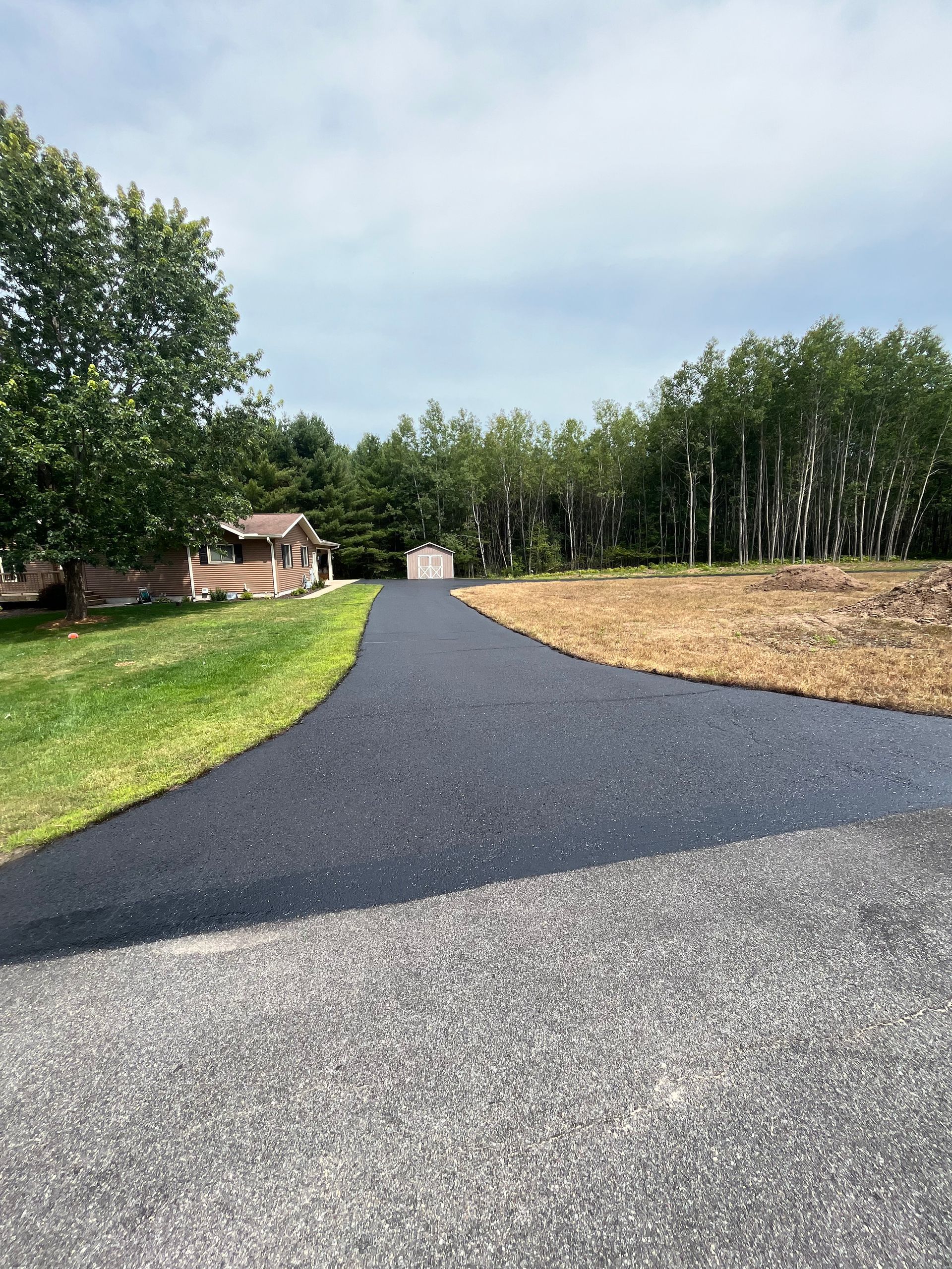 A driveway with a house in the background and trees on the side